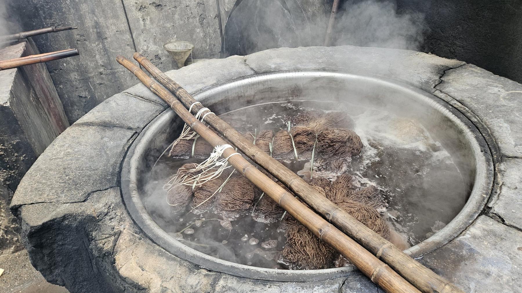 Wool submerged in a steaming dye vat over an open fire in the Rug Gossips dye house, Lahore